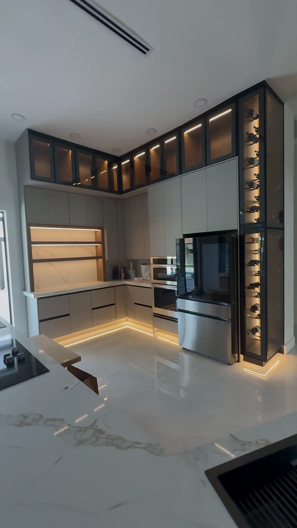 Modern custom kitchen with gray cabinetry, glass-front upper cabinets, integrated lighting and black appliances.