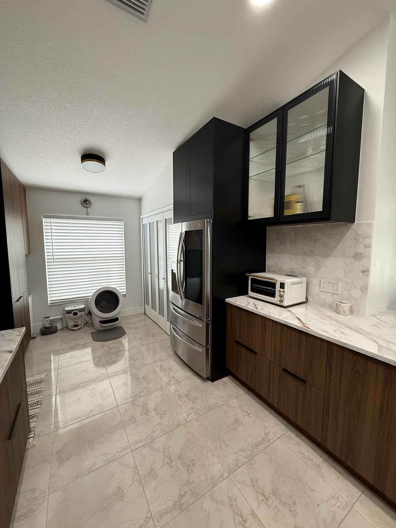 Compact renovated kitchen with black glass-front upper cabinets, warm wood lower cabinetry and stone counters.